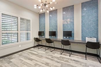 A room with a long desk with three computers on it and a chandelier hanging from